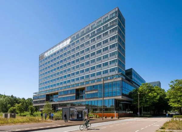 Modern kantoorgebouw genaamd Adam Smith Building aan de Thomas R. Malthusstraat met glazen gevel en mensen op straat.